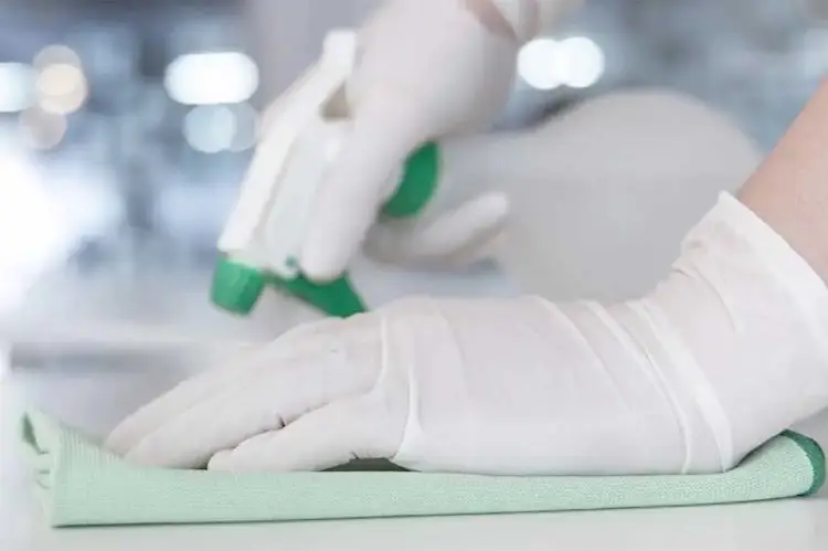 Hände in Gummihandschuhen reinigen Fläche mir Sprühflasche und Lappen.