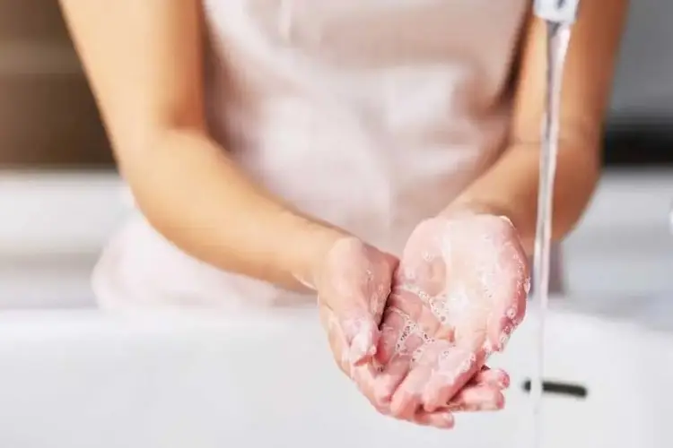 Eingeseifte Hände unter einem Wasserstrahl an einem Waschbecken.